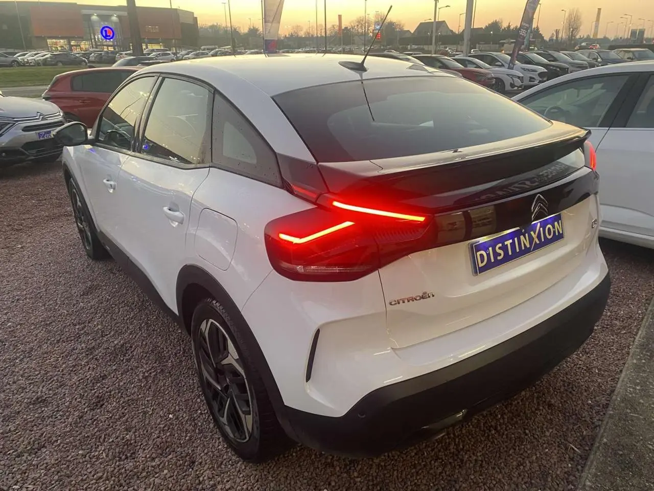 Vue 3/4 arrière droite d'une Citroën C4 blanche de 2021 avec feux arrière allumés et toit noir contrastant.
