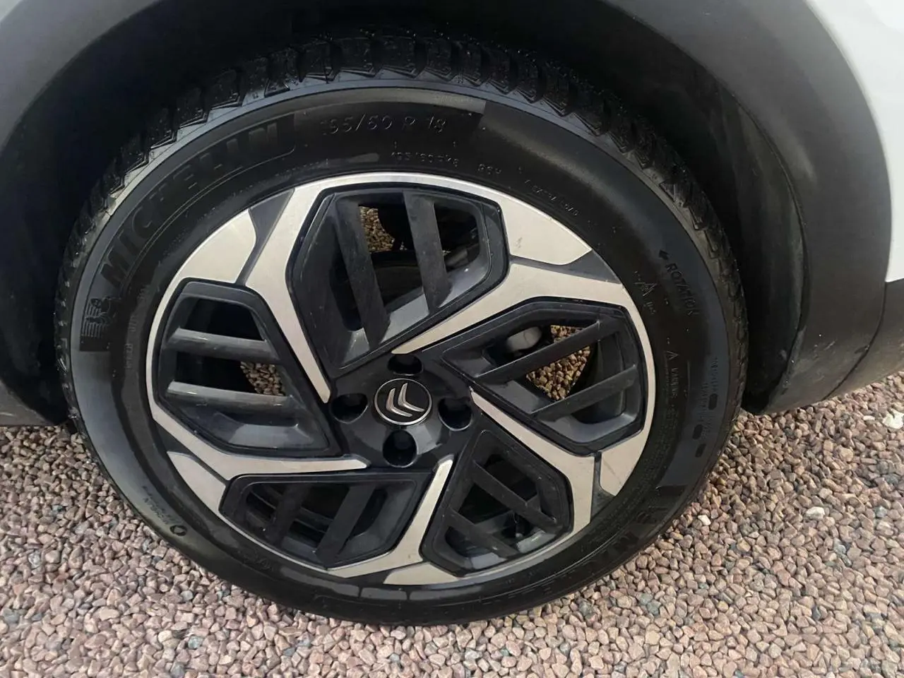 Gros plan sur la roue avant droite d'une Citroën C4 blanche avec jante alliage noire et argentée au design géométrique.