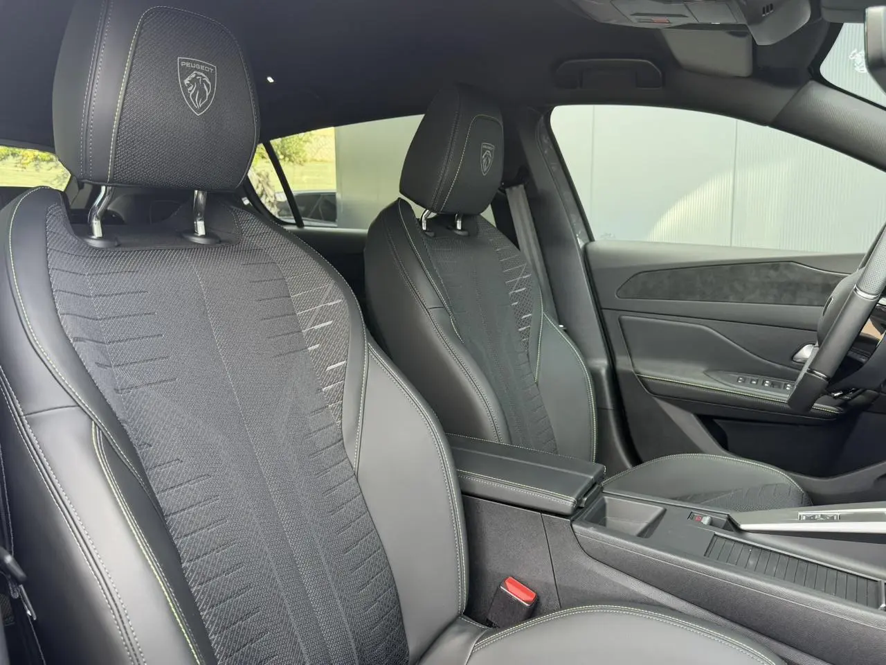 Vue intérieure côté droit des sièges avant noirs avec surpiqûres vert Adamite et logo Peugeot embossé sur appuie-têtes.