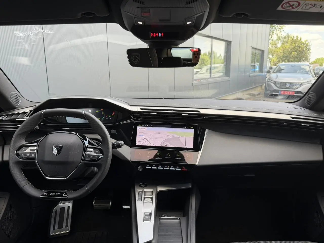 Vue intérieure avant de la Peugeot 308 GT Hybrid 2026 avec volant compact cuir noir et écran tactile central.
