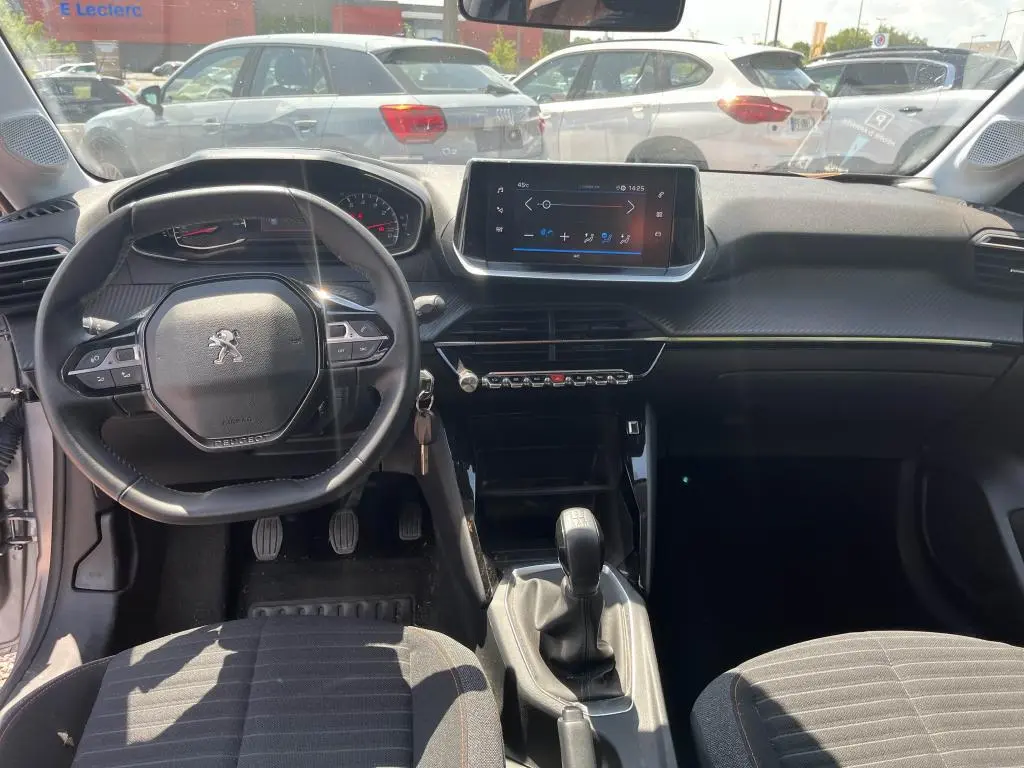 Vue intérieure avant de la Peugeot 208 gris clair 2023, avec volant compact, écran tactile et boîte manuelle visible.