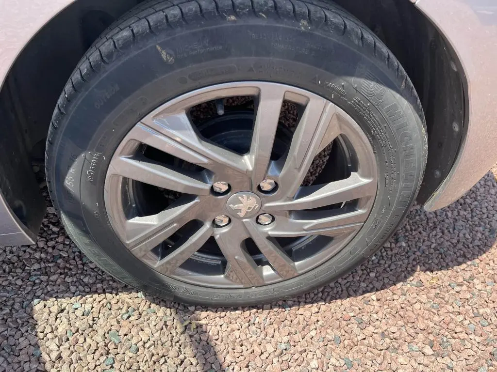 Gros plan sur la roue avant droite d'une Peugeot 208 gris clair 2023 avec jante alliage et logo lion au centre.