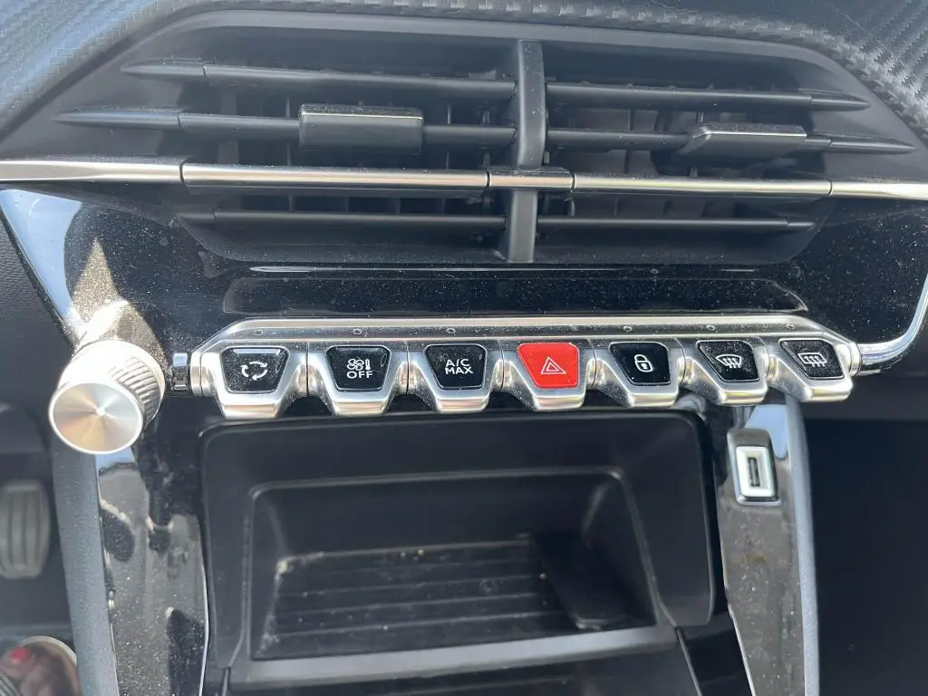 Vue rapprochée des commandes centrales chromées et boutons fonctionnels sur tableau de bord noir brillant d’une Peugeot 208 gris clair 2023.