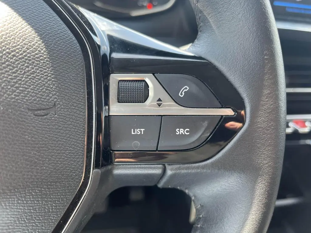 Gros plan sur les commandes gauche du volant noir du Peugeot 208 gris clair 2023, avec boutons LIST, SRC et téléphone.