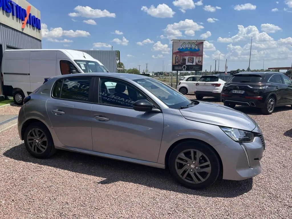 Peugeot 208 gris clair vue de profil côté gauche sur parking extérieur avec jantes alliage et calandre distinctive.