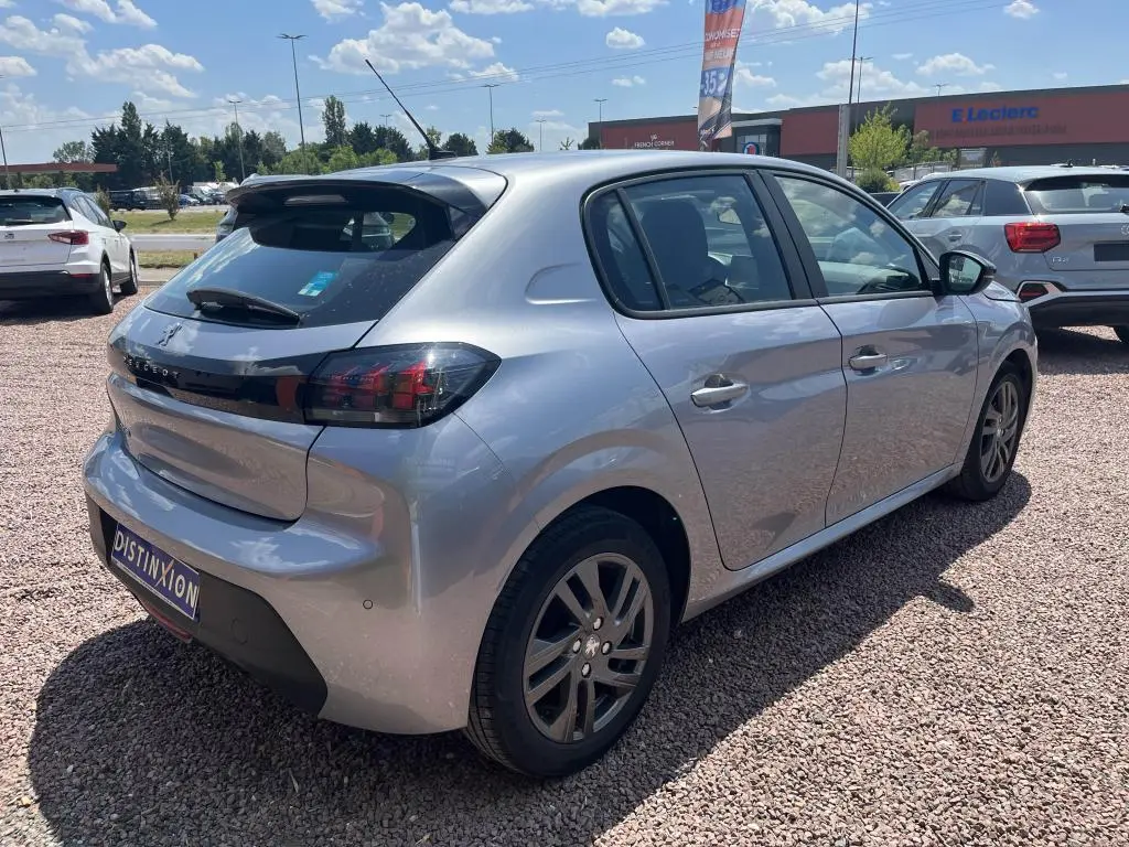 Peugeot 208 gris clair vue 3/4 arrière droit, avec feux arrière noirs et jantes alliage, stationnée sur gravier.