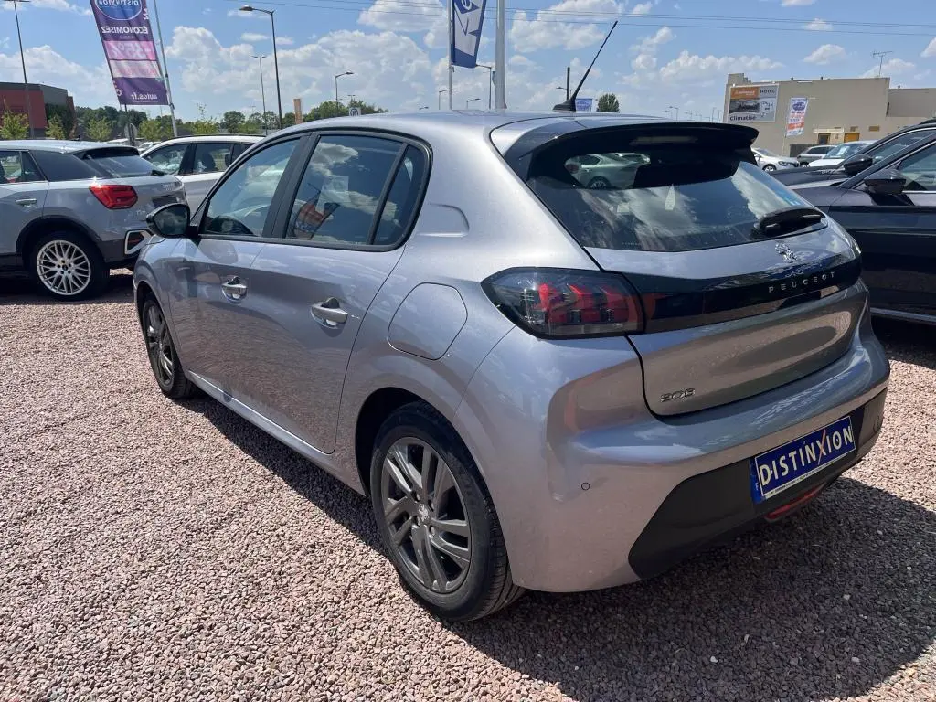 Peugeot 208 gris clair vue 3/4 arrière droit, avec feux arrière noirs et toit légèrement surélevé, en extérieur sur parking.