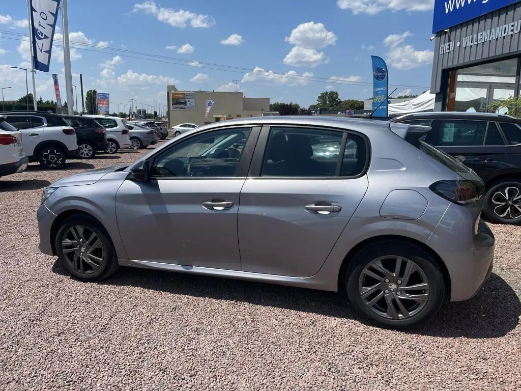 Peugeot 208 gris clair vue de profil côté gauche, avec jantes alliage et toit légèrement incliné vers l'arrière.