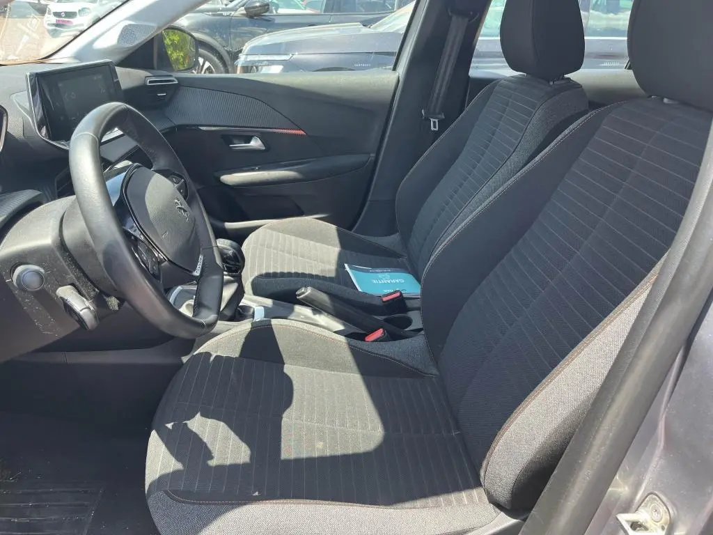 Vue intérieure côté conducteur de la Peugeot 208 1.2i PureTech 75 Active Pack 2023 avec sièges tissu noirs et volant compact.