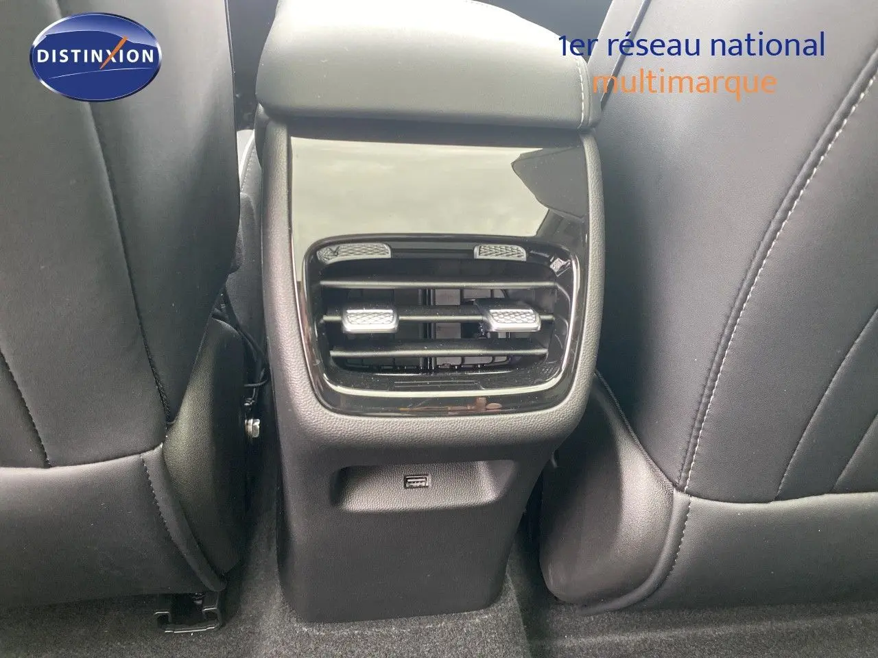Détail de la console arrière avec sorties d’air noires et port USB, entre sièges avant en cuir noir.