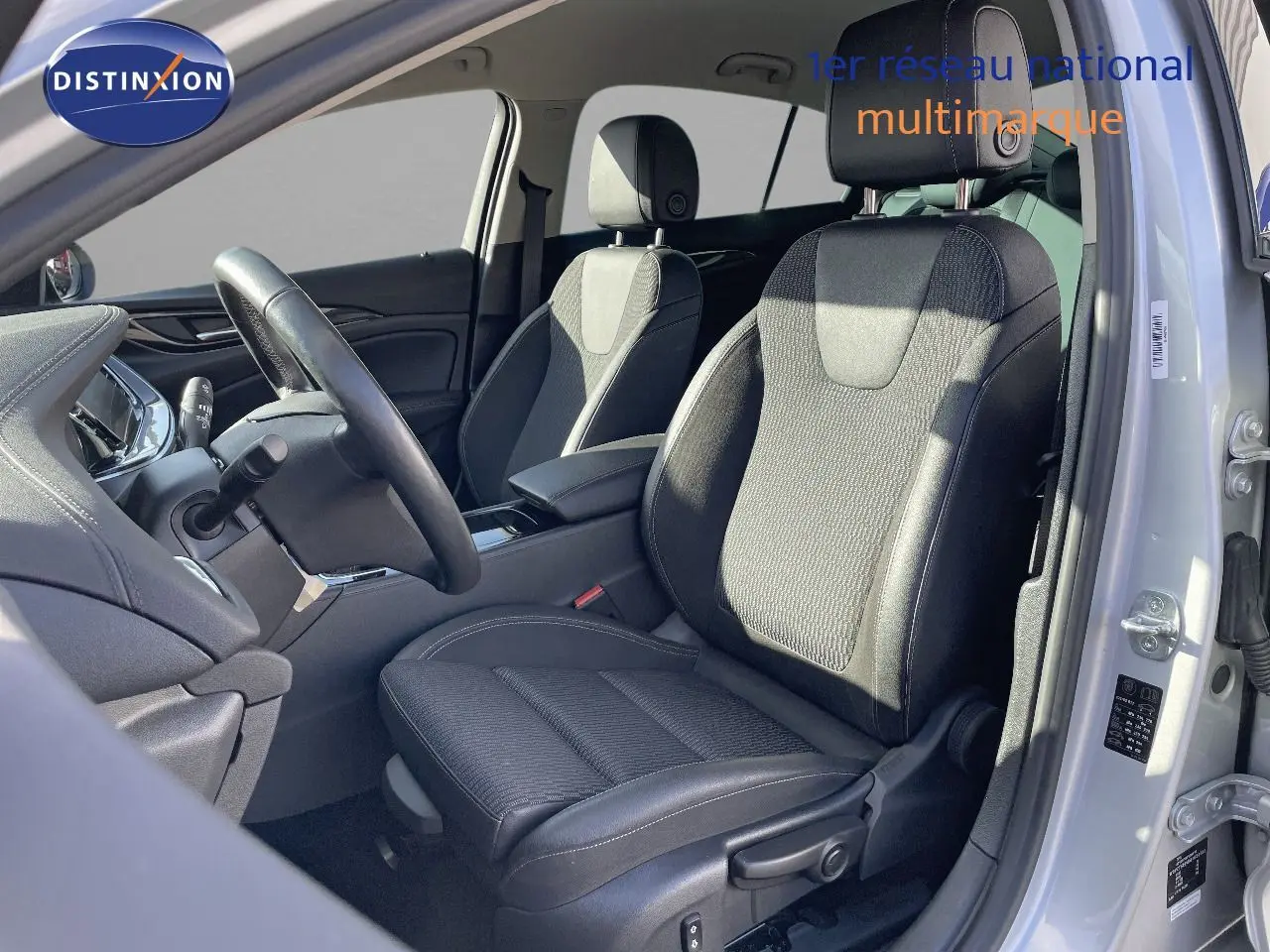 Vue intérieure côté conducteur de l'Opel Insignia 2021 avec sièges tissu noir et gris, volant et tableau de bord visibles.