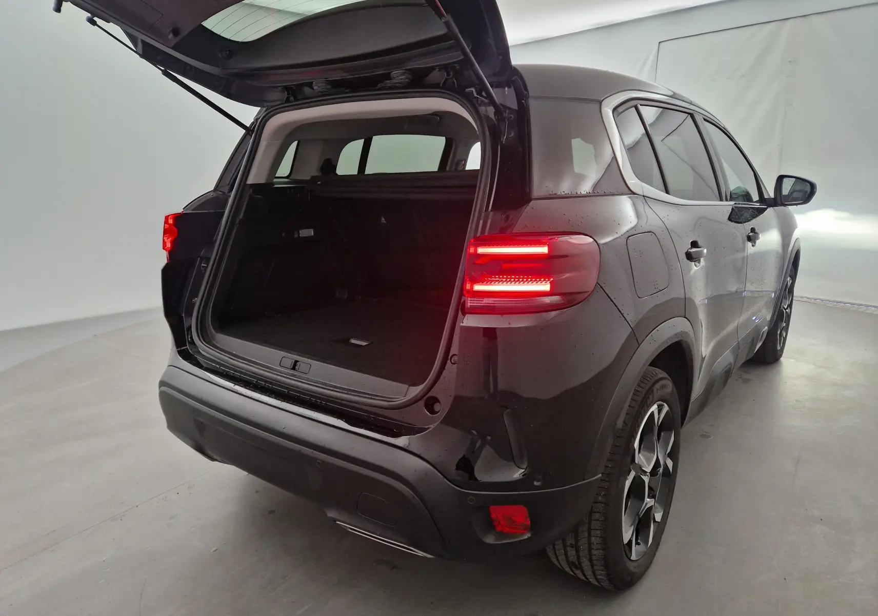 Vue 3/4 arrière droite du Citroën C5 Aircross noir 2024 avec coffre ouvert et feux arrière allumés.