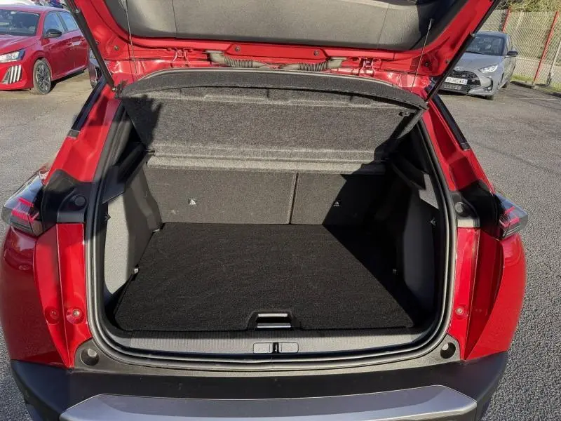 Coffre ouvert vu de l'arrière du Peugeot 2008 rouge Elixir avec intérieur noir et hayon levé.