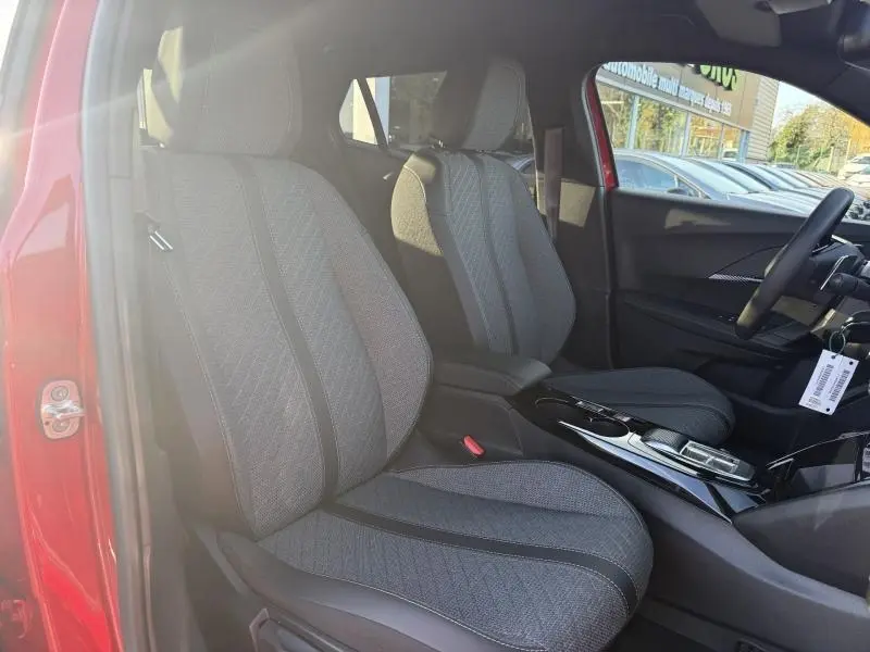 Vue intérieure côté gauche du Peugeot 2008 rouge Elixir, sièges tissu gris avec console centrale brillante noire.