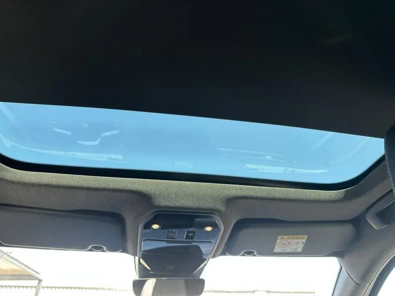 Vue intérieure du toit ouvrant panoramique du Renault Austral 2025, avec commandes intégrées et ciel bleu visible.