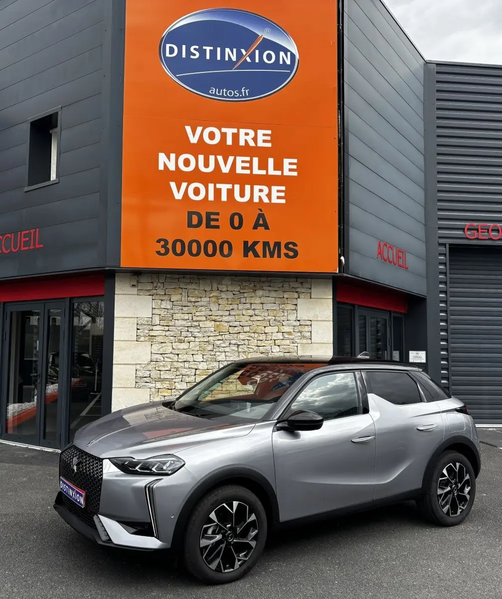 DS3 gris clair vue 3/4 avant droit, avec toit noir et jantes alliage distinctives, devant un panneau orange Distinxion.