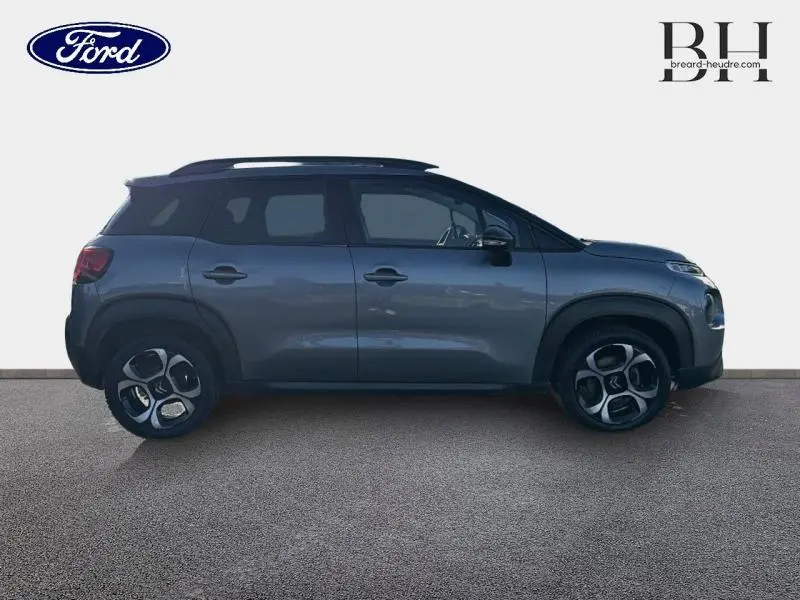 Vue de profil côté gauche d'une Citroën C3 Aircross gris acier avec barres de toit et jantes diamantées.