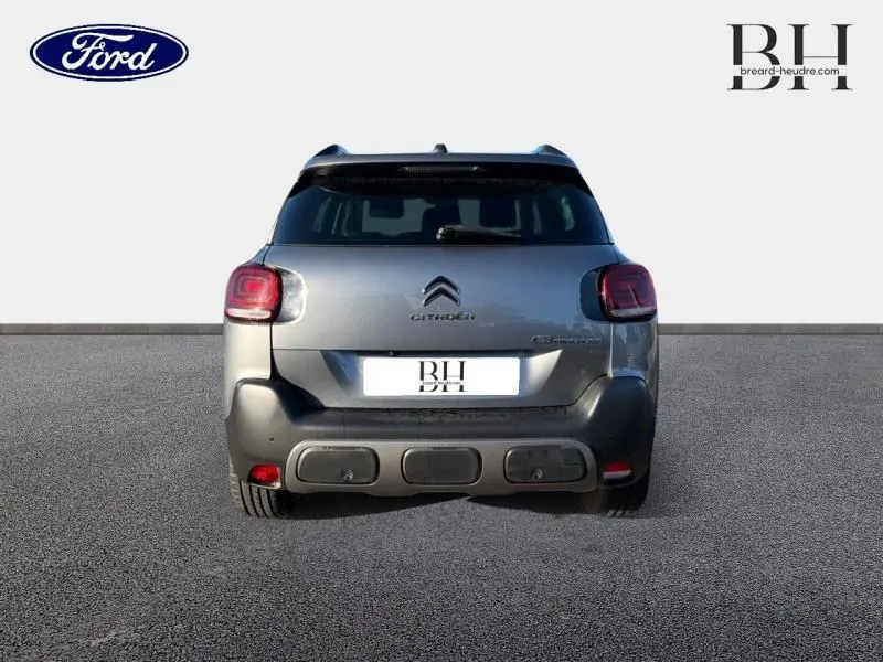 Vue arrière d'un Citroën C3 Aircross gris acier avec feux arrière carrés et barres de toit visibles.