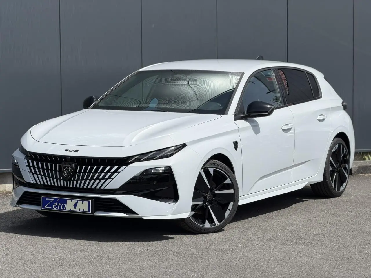 Peugeot 308 NV Hybrid blanc Okenite vue 3/4 avant droit avec jantes noires bi-tons et calandre distinctive.