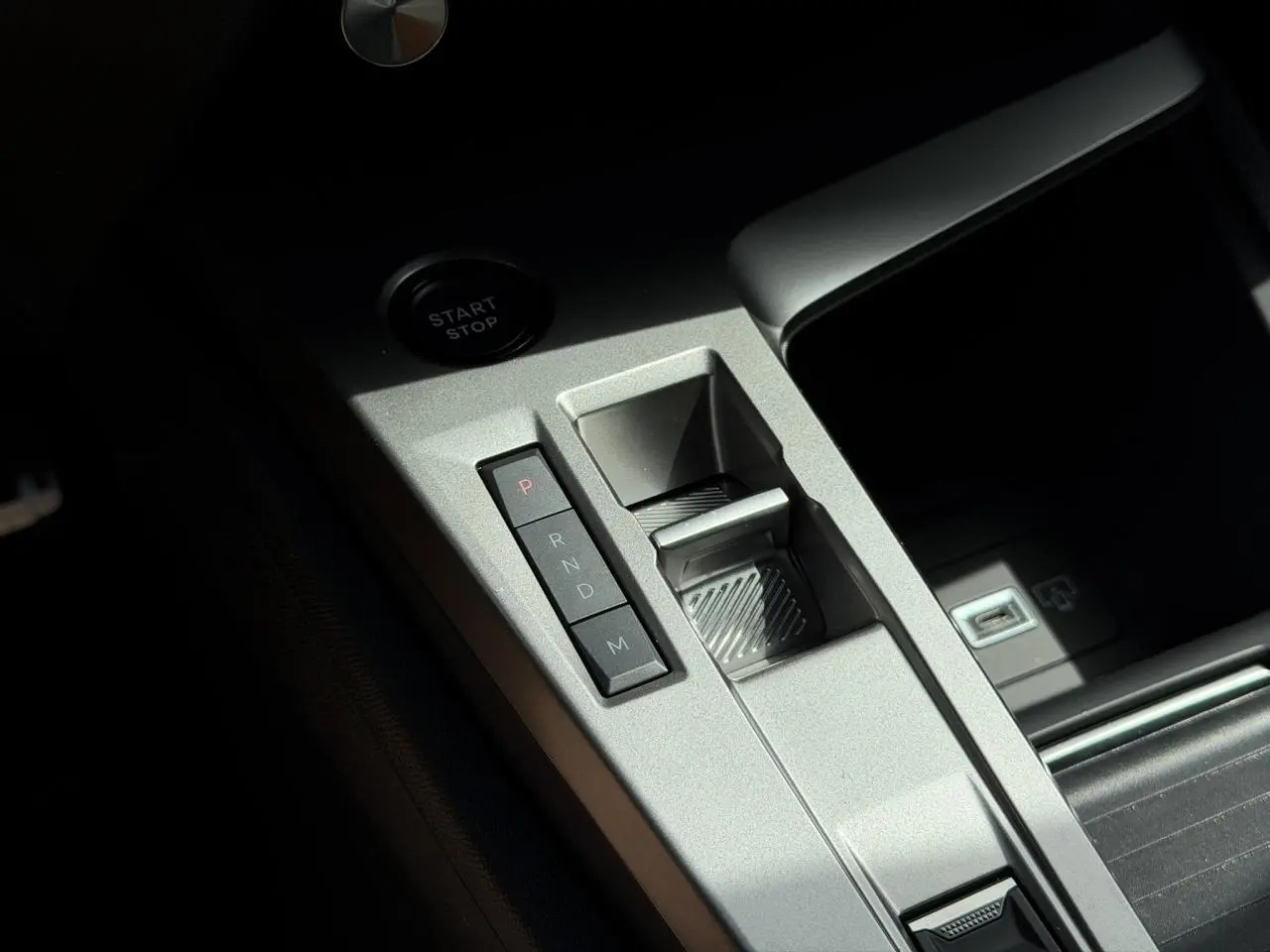 Gros plan sur la console centrale grise avec commandes de boîte auto et bouton start/stop du Peugeot 308 Hybrid blanc.