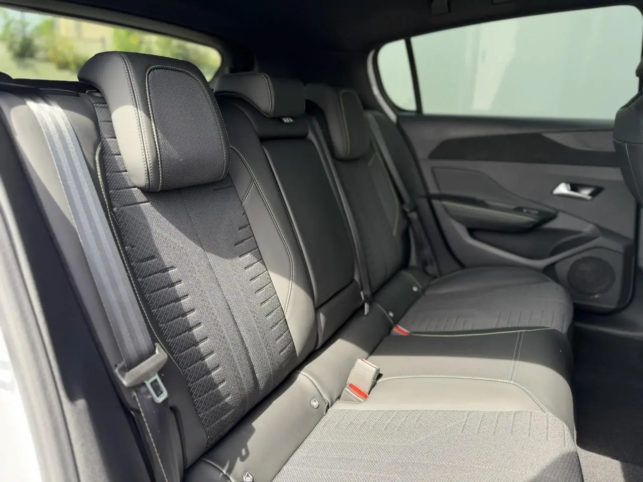 Vue latérale intérieure montrant la banquette arrière tissu noir avec surpiqûres vert Adamite de la Peugeot 308 Hybrid 2026.
