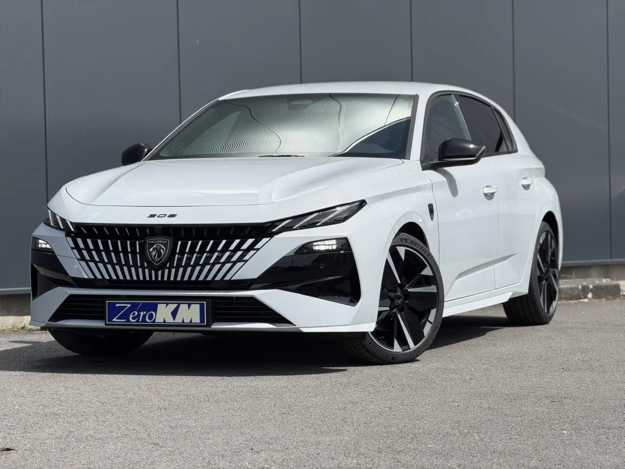 Vue 3/4 avant droite d'une Peugeot 308 blanche Okenite avec calandre noire distinctive et jantes alliage bi-ton.