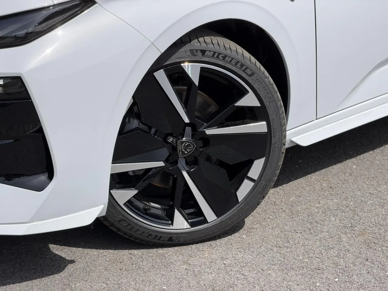 Gros plan sur la roue avant droite de la Peugeot 308 NV Hybrid blanche avec jante alliage bi-ton noir brillant et argent.