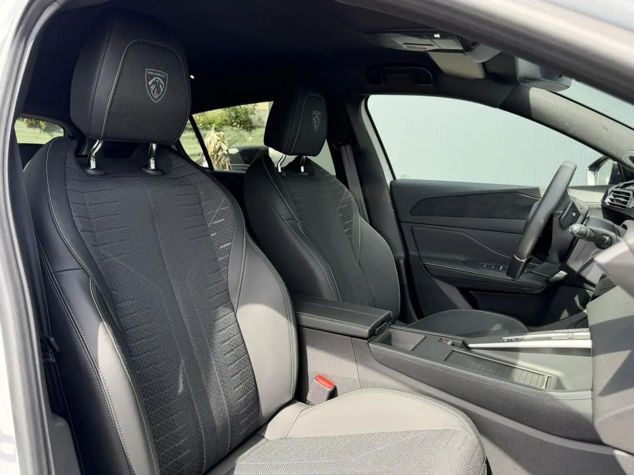 Vue intérieure côté conducteur de la Peugeot 308 NV Hybrid 145 GT avec sellerie noire et surpiqûres vert Adamite.