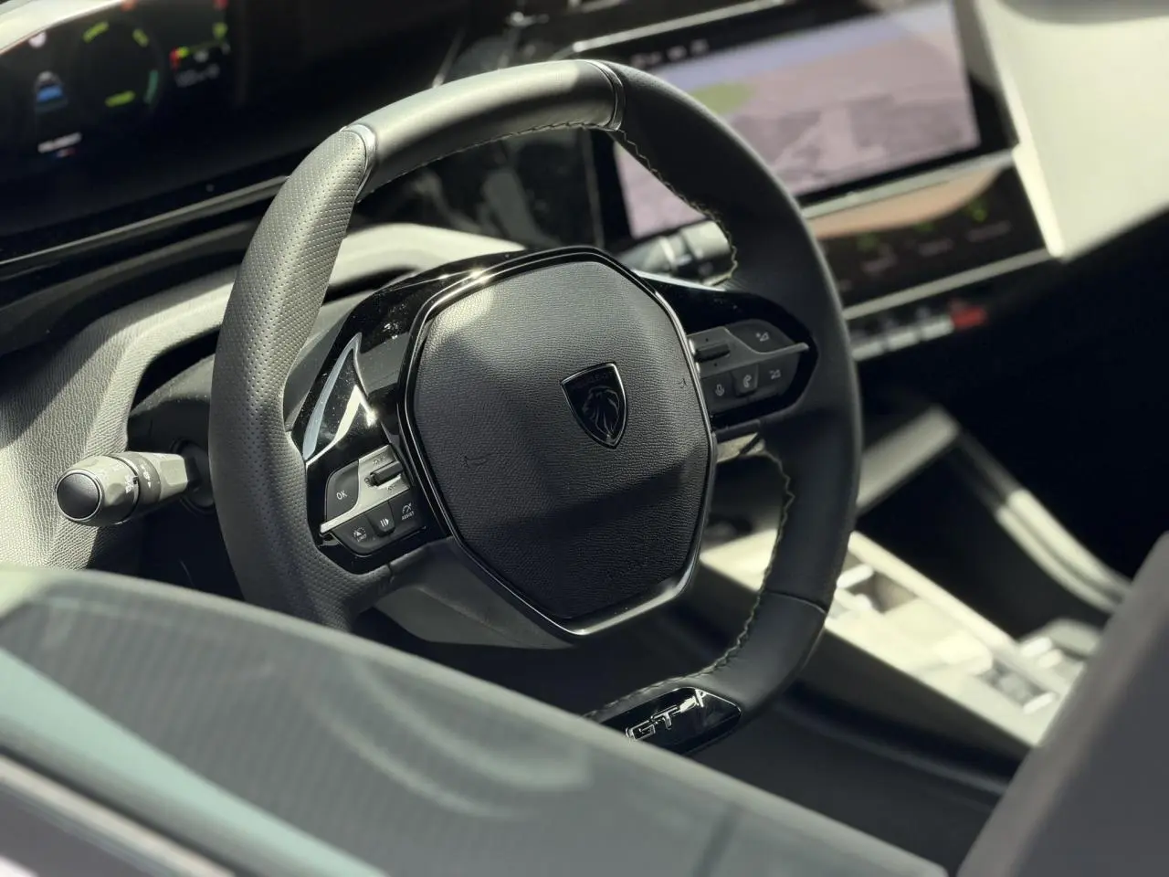 Gros plan sur le volant cuir noir GT avec logo Peugeot, tableau de bord numérique et écran tactile du Peugeot 308 Hybrid.