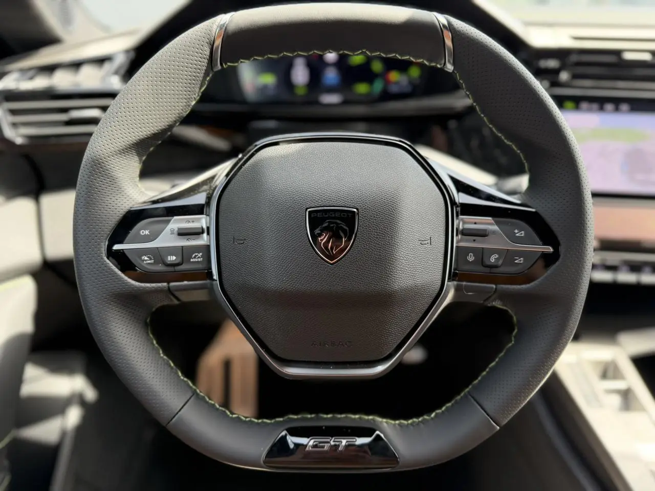 Gros plan sur le volant cuir noir du Peugeot 308 GT avec surpiqûres vertes et logo central lion brillant.