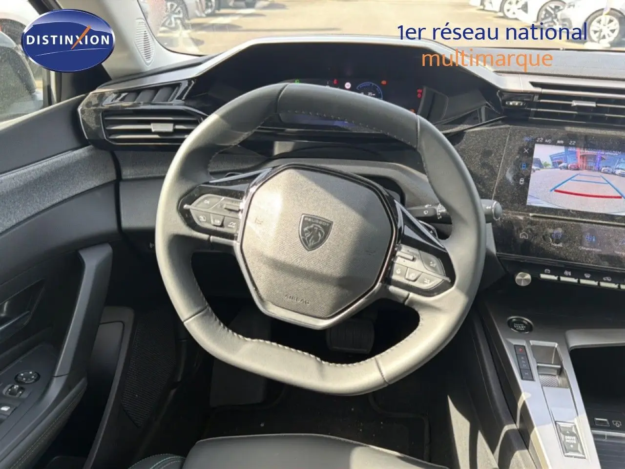 Vue intérieure centrée sur le volant cuir du Peugeot 308 Allure Hybrid 2025 avec écran tactile et caméra de recul affichée.
