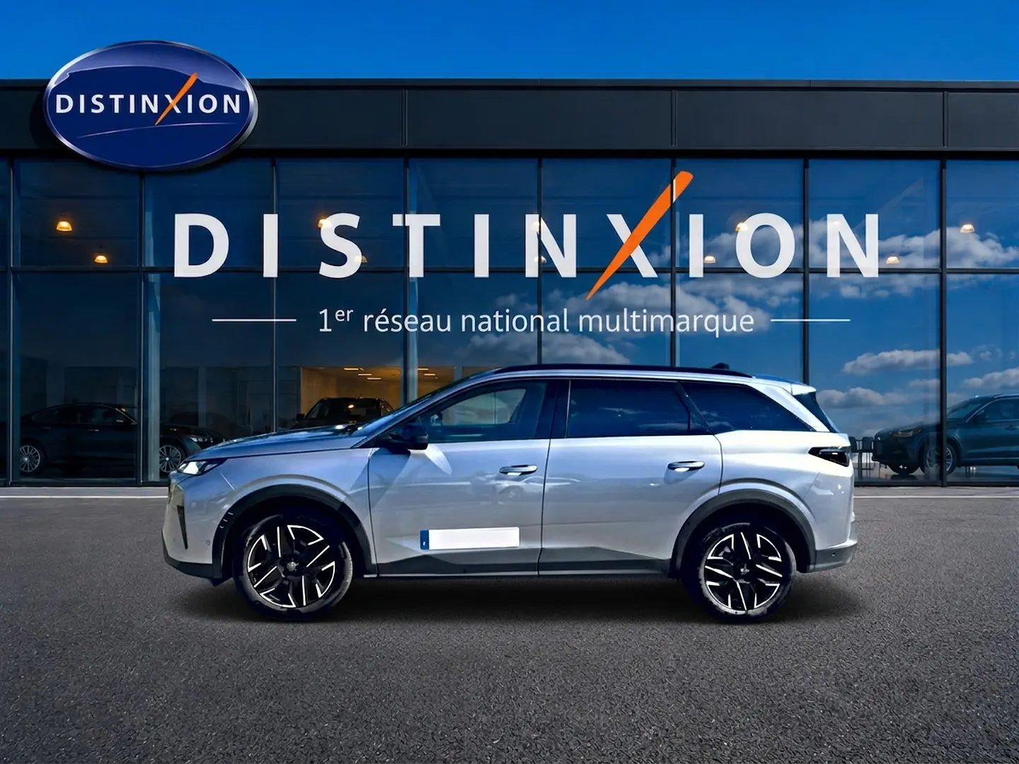 Vue latérale droite du Peugeot 5008 Hybrid 145 allure e-dcs6 gris artense avec jantes alu devant une vitrine Distinxion.