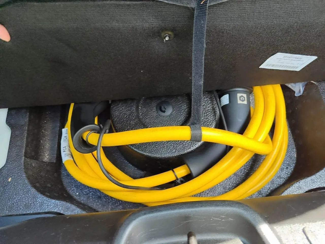 Câble de recharge électrique jaune enroulé dans le coffre d'une Fiat 500 électrique blanche, vue en plongée.