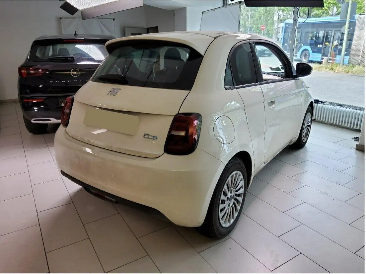 Vue 3/4 arrière droite d'une FIAT 500 électrique blanche 2024 dans un showroom avec feux arrière foncés.