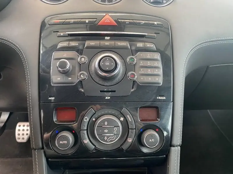 Vue rapprochée de la console centrale noire brillante du Peugeot RCZ 1.6 THP avec commandes audio et climatisation automatique.