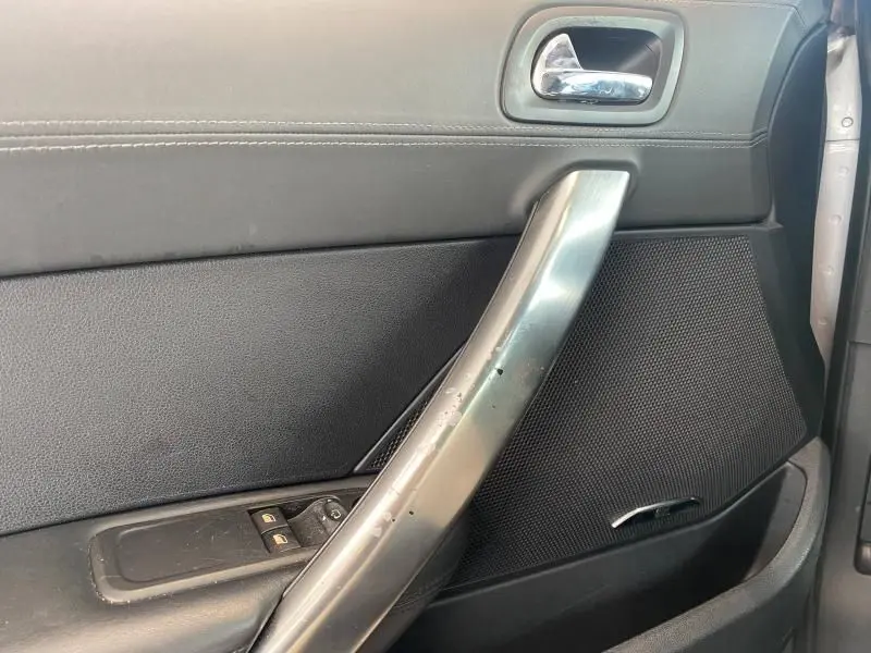 Détail de la porte intérieure côté gauche d'une Peugeot RCZ gris avec poignée métallique et commandes de vitres électriques.