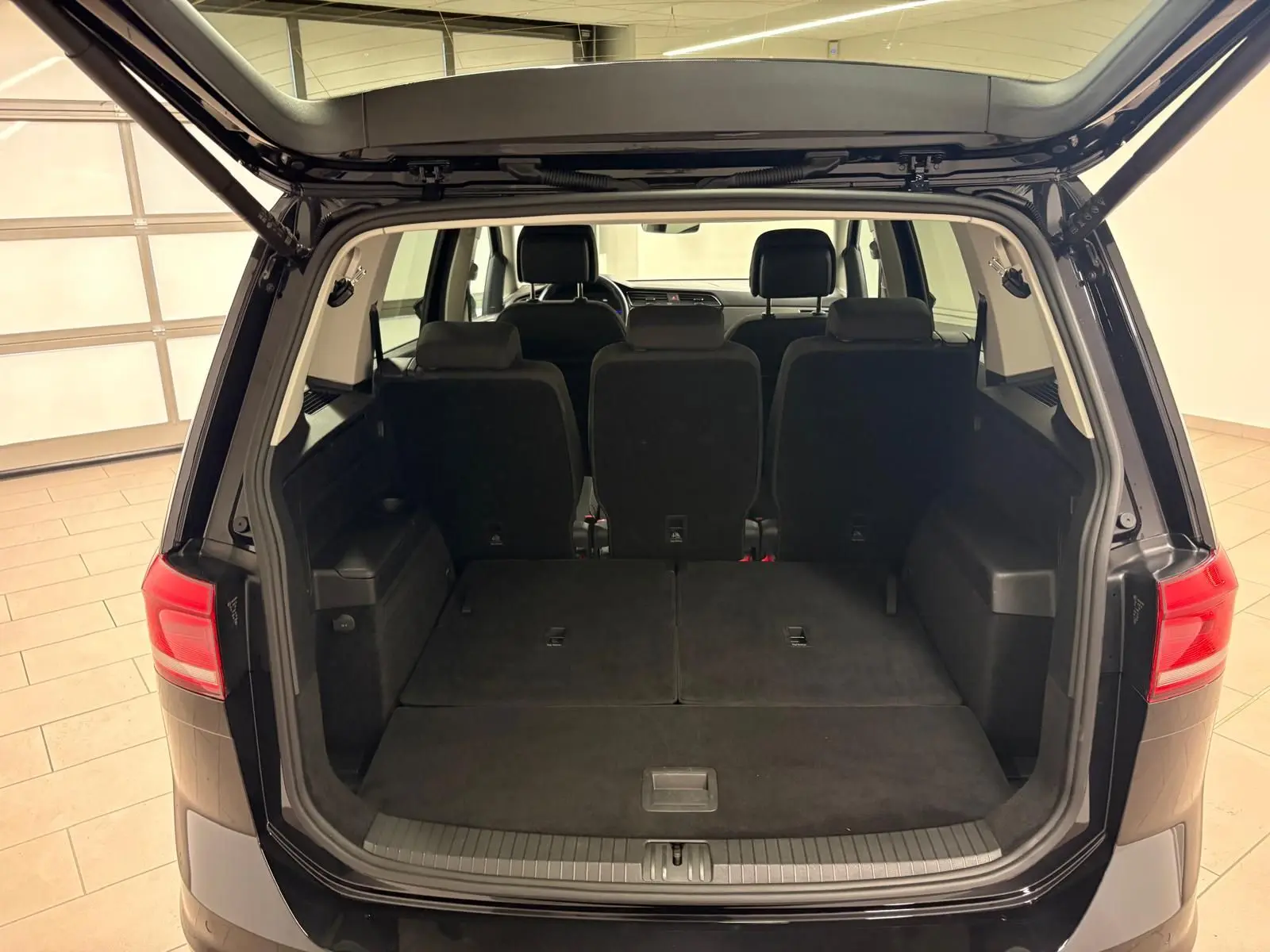 Coffre ouvert d'un Volkswagen Touran noir intense nacré, vue arrière montrant les sièges arrière et l'espace de chargement.
