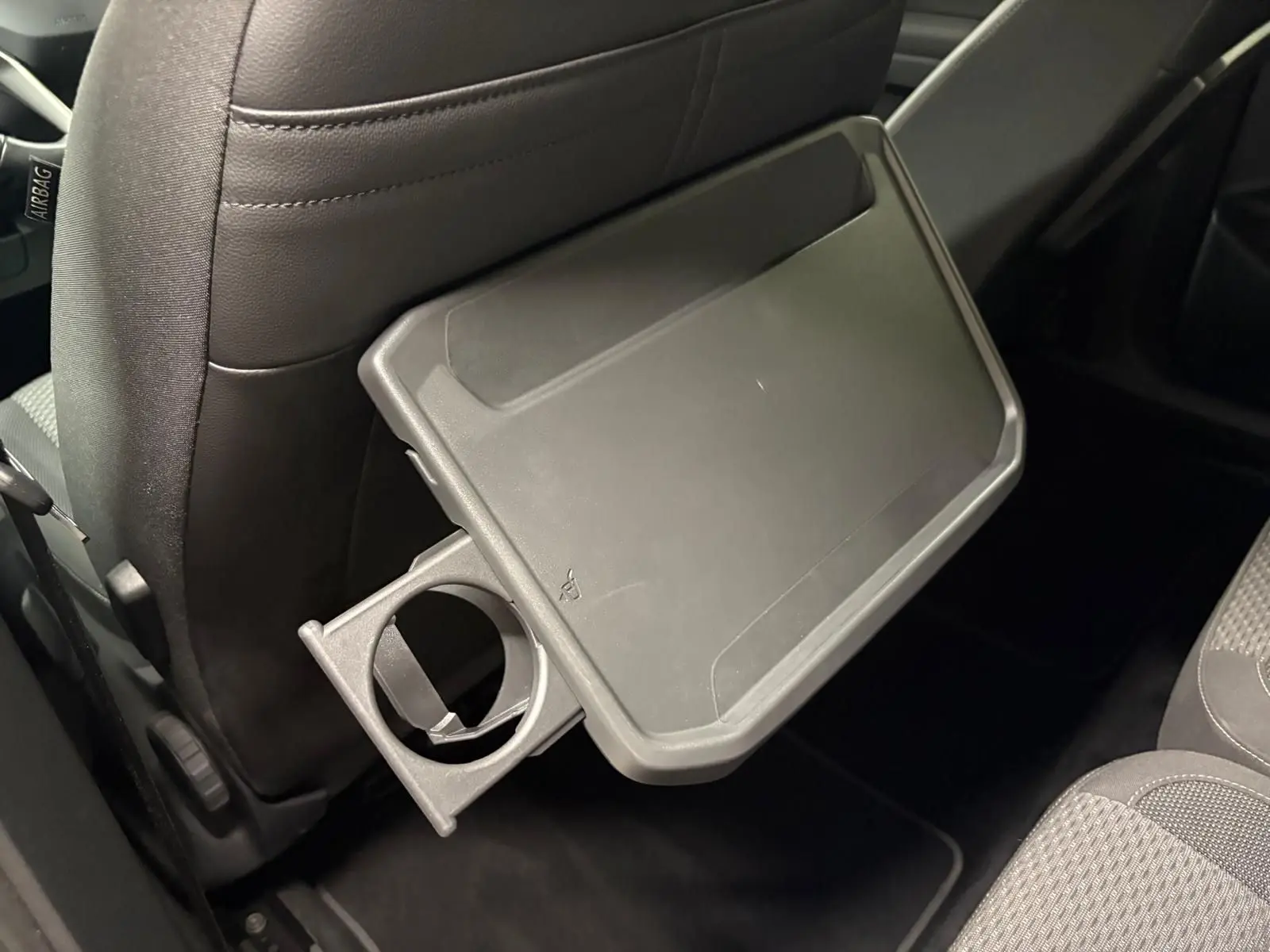 Tablette rabattable avec porte-gobelet intégrée au dos du siège avant dans l'habitacle du Volkswagen Touran noir intense nacré.