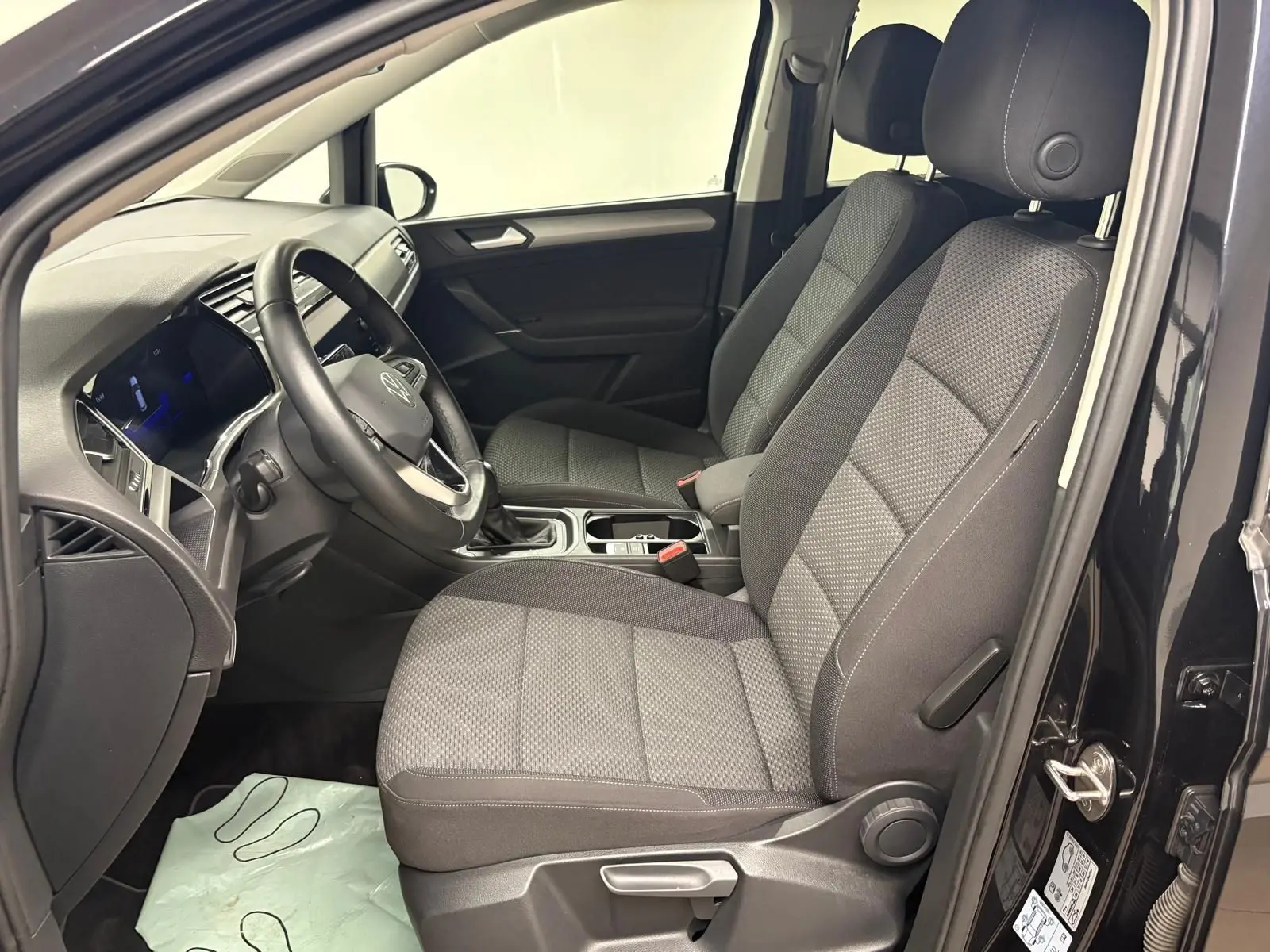 Intérieur avant droit du Volkswagen Touran noir intense nacré, sièges tissu gris et tableau de bord moderne.