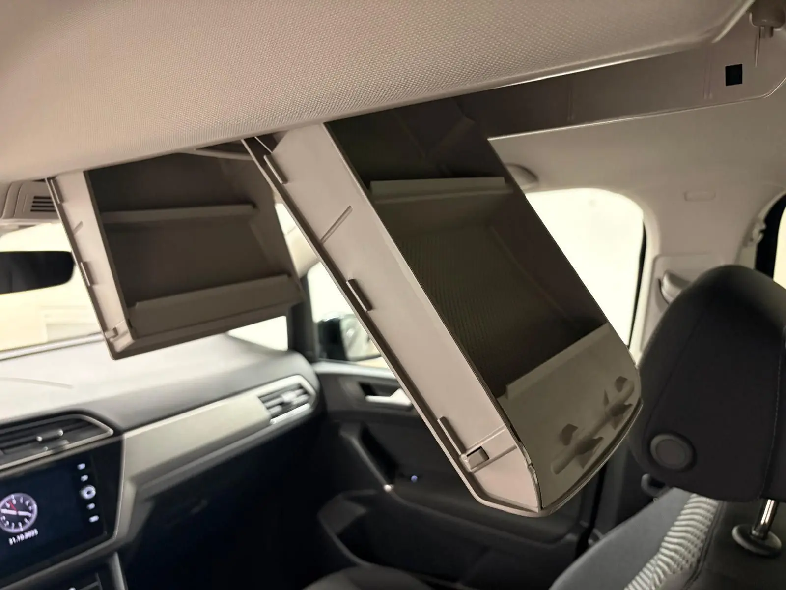 Vue intérieure du Volkswagen Touran 2024, coffre à lunettes ouvert au-dessus des sièges avant noirs.