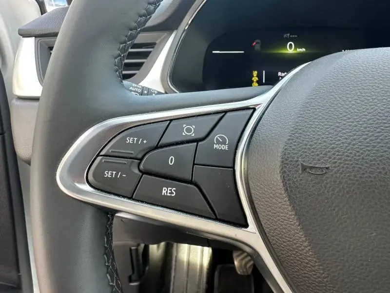 Gros plan sur les commandes du volant côté gauche du Renault Captur blanc nacré 2025, avec boutons de régulateur de vitesse.