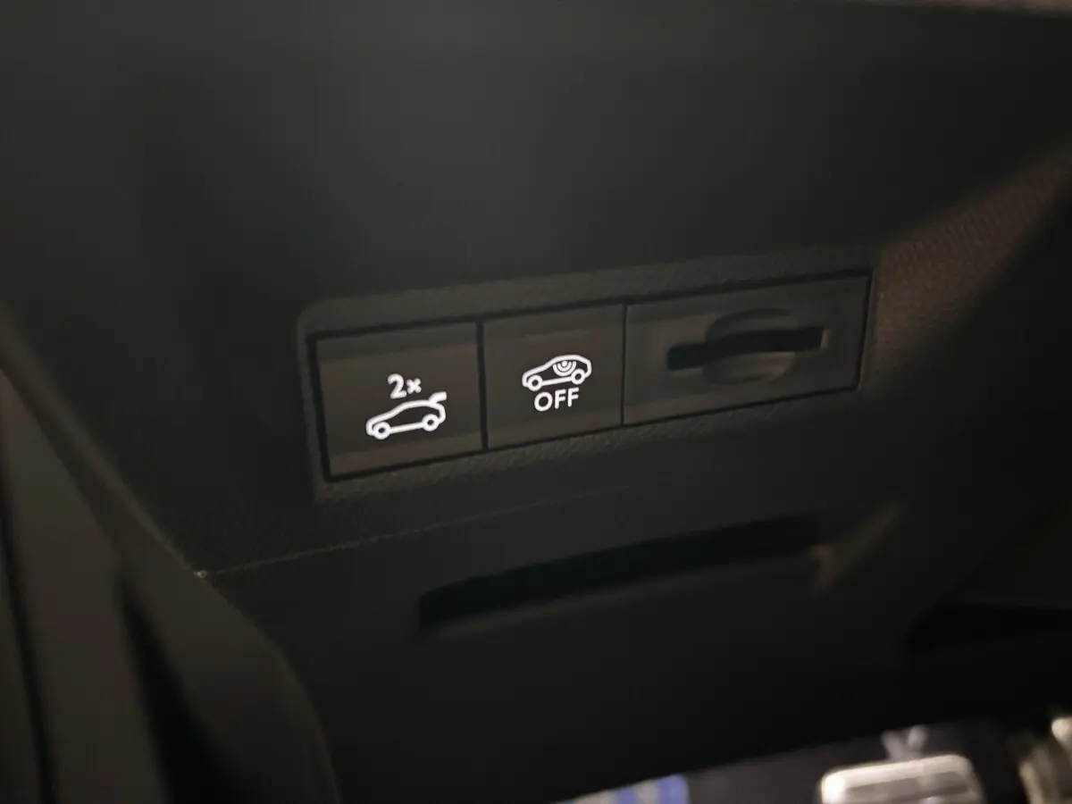 Gros plan sur les boutons de commande intérieurs du Peugeot 3008 hybride 2025, avec éclairage blanc sur fond noir.