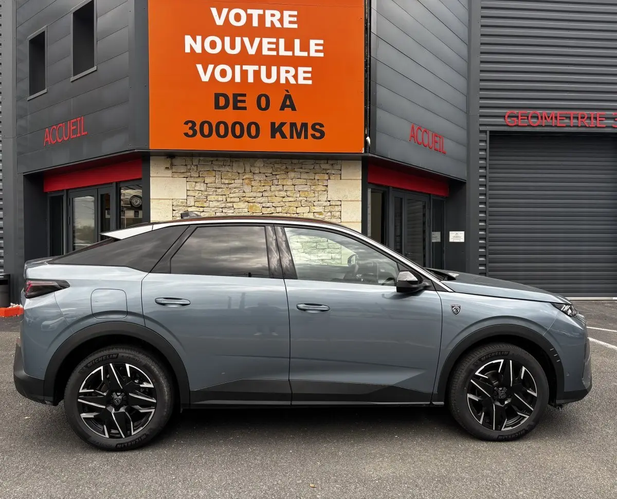 Profil droit d'un Peugeot 3008 gris métallisé, avec jantes noires et toit noir, stationné devant un bâtiment commercial.