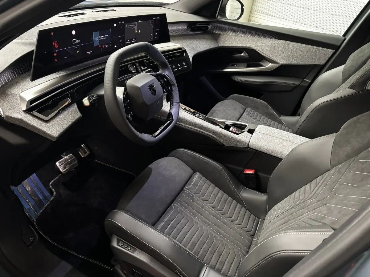 Vue intérieure côté conducteur du Peugeot 3008 1.2 HYBRID 145 GT, avec tableau de bord numérique et sièges en cuir noir et tissu gris.