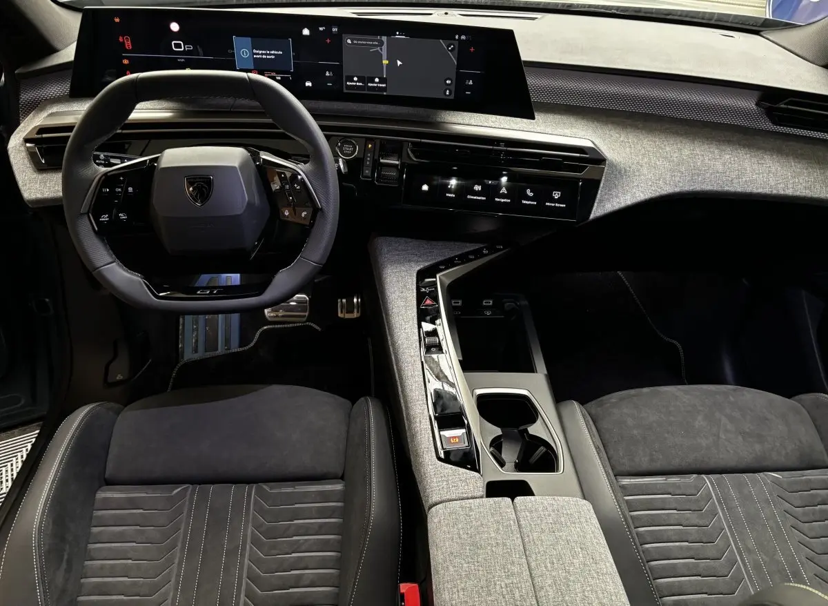 Vue intérieure avant du Peugeot 3008 1.2 Hybrid 145 GT, volant cuir GT, sièges tissu noir et console centrale grise.