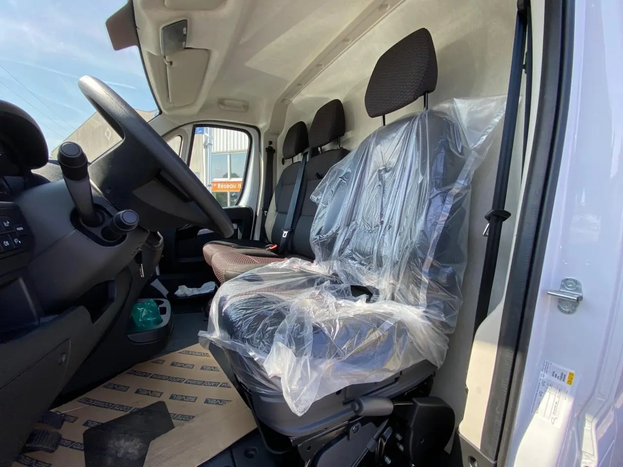 Vue intérieure côté conducteur du Citroën Jumper blanc 2023, sièges avant avec protection plastique et volant visible.