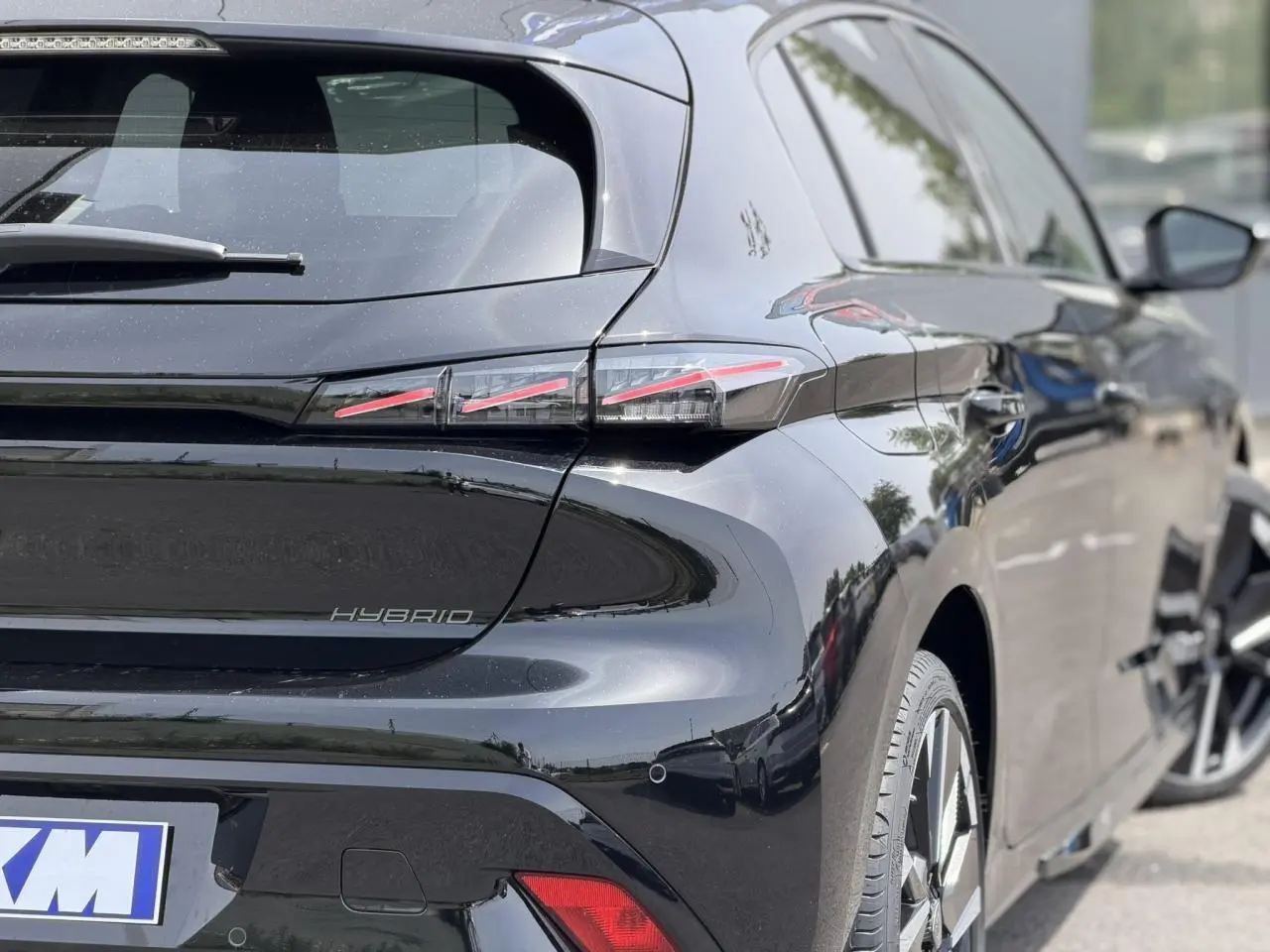Vue 3/4 arrière droite de la Peugeot 308 NV Hybrid 145 GT e-DSC6 noir Perla avec feux arrière LED 3 griffes et jantes alliage bi-tons.