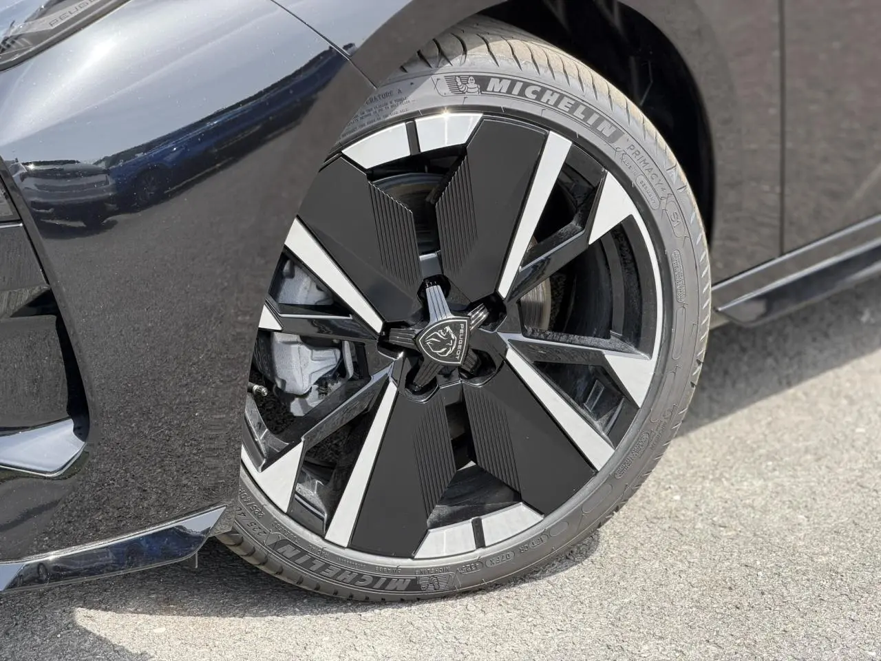 Gros plan sur la jante alliage 18" bi-tons noir et argent avec logo Peugeot, sur la roue avant droite noire Perla.