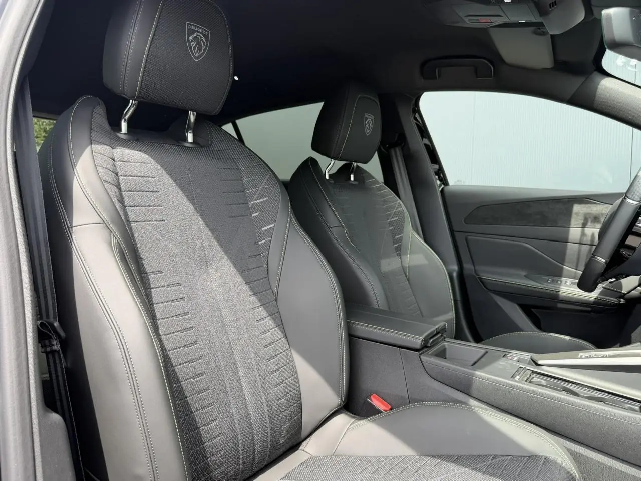 Vue intérieure côté gauche des sièges avant noirs avec surpiqûres vertes et logo Peugeot embossé sur appuie-têtes.