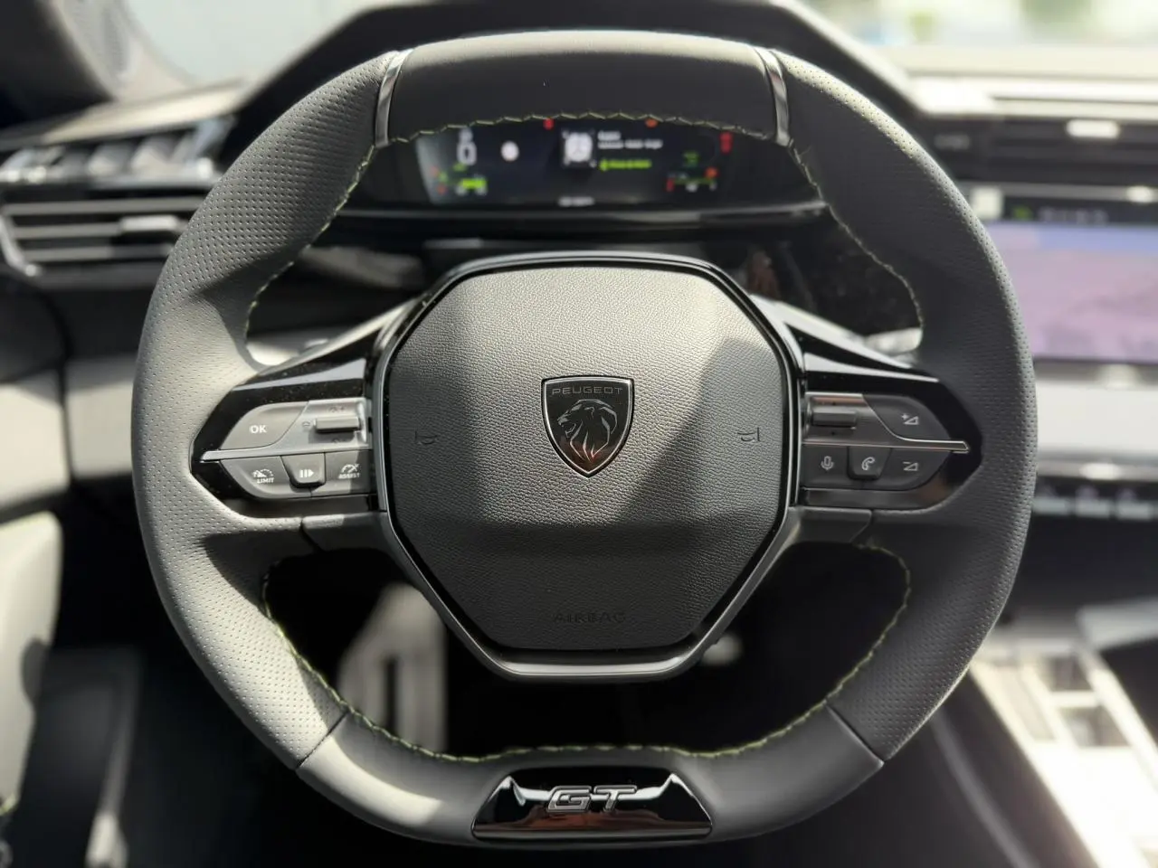 Vue rapprochée du volant compact GT en cuir noir avec surpiqûres vert Adamite et logo Peugeot au centre.